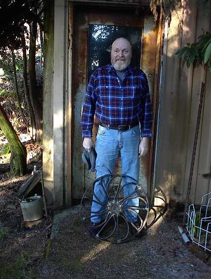 Man standing at shed doorway holding an old wagon wheel