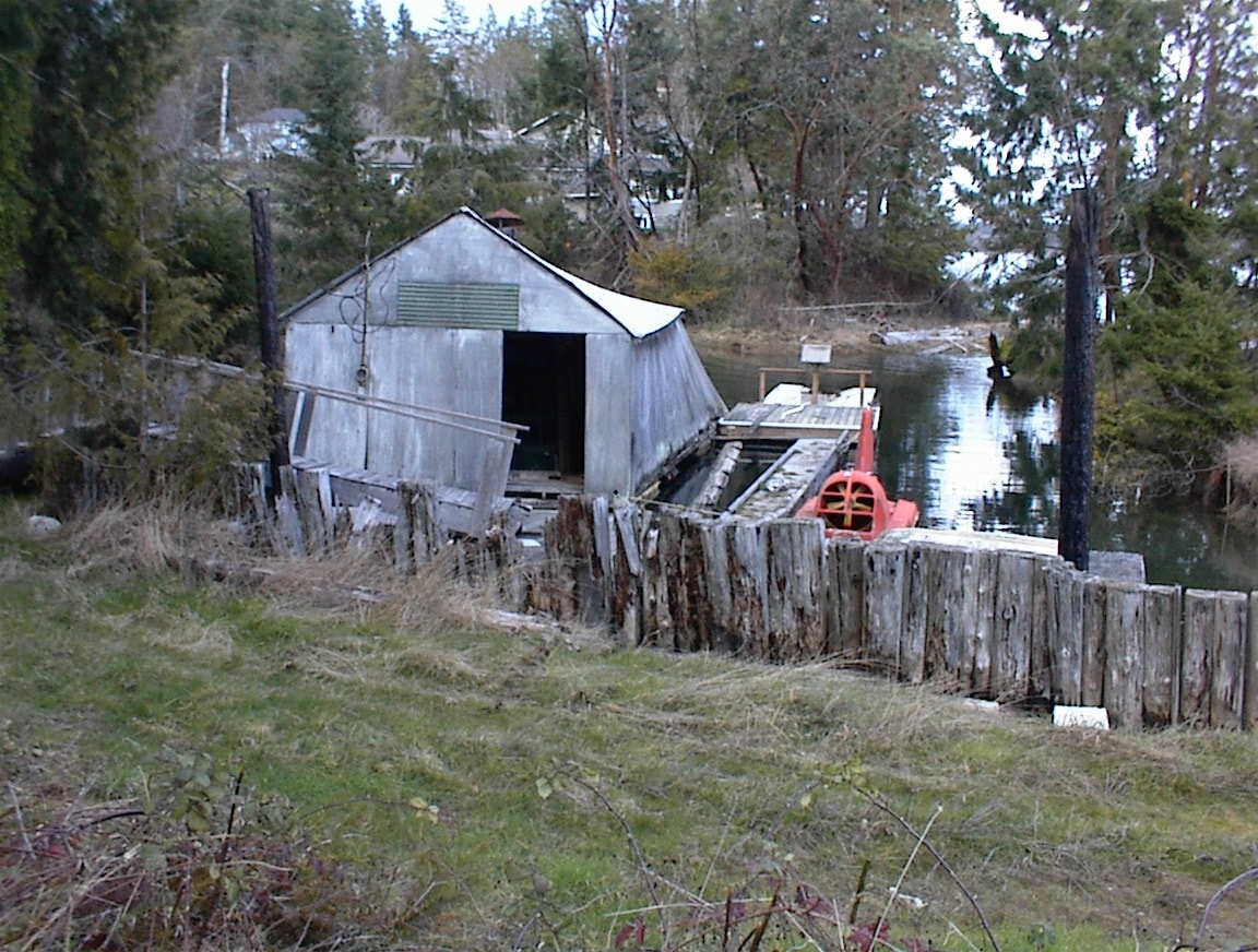 Weathered old boathouse on forested waterfront with red machinery visible