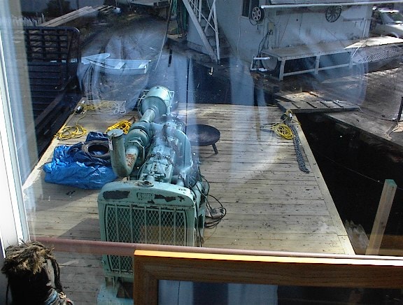 Engine and machinery on a wooden dock floor viewed through a window