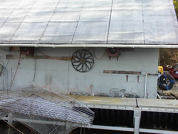 Side of a metal-roofed building with a wheel and equipment mounted on the wall